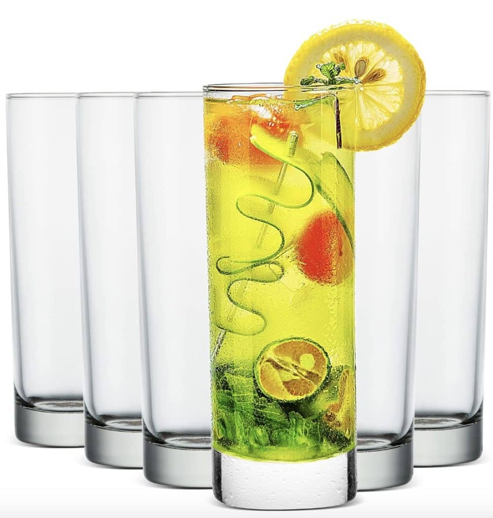 A row of five tall, clear glasses, with the middle one filled with a bright yellow beverage. This easy summer mocktail recipe boasts ice, cucumber spirals, lime, and is garnished beautifully with a lemon slice and a sprig of herbs.